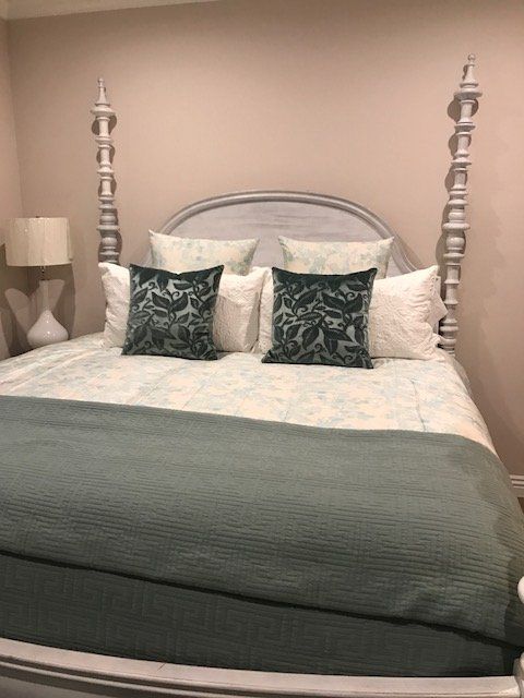 A bed with a white headboard and posts, covered in blue and green bedding and pillows, with a lamp on the side.