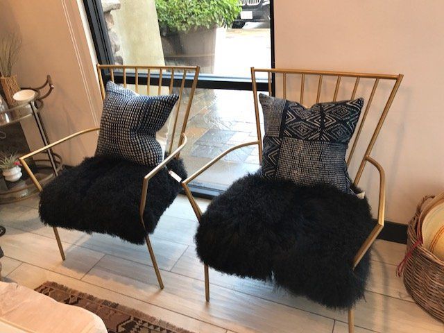 Two modern gold metal chairs with black fur throws and patterned pillows.