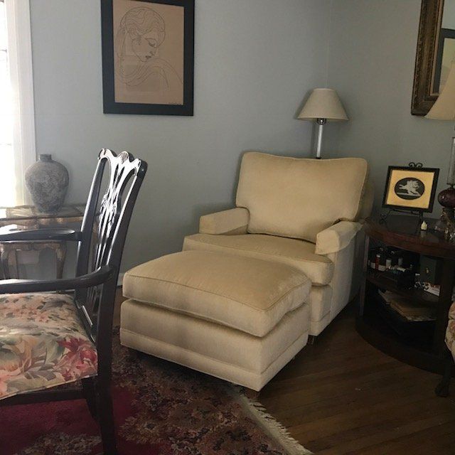 Cozy living room with a cream-colored armchair and ottoman, a floral chair, and artwork.