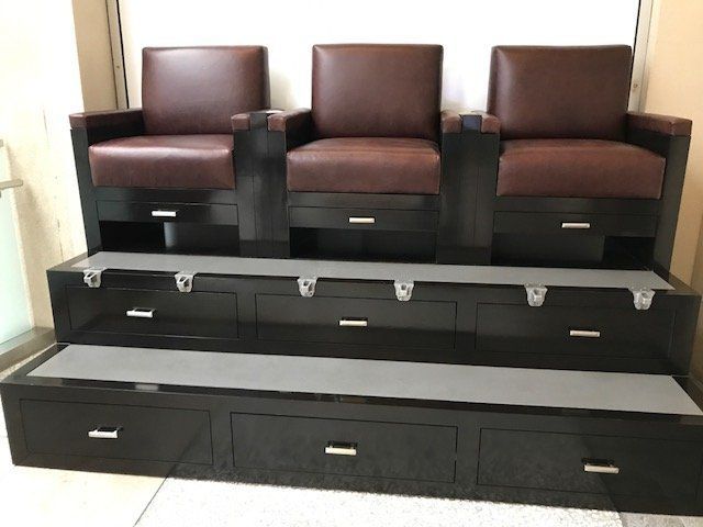 Dark wood salon station with three brown leather chairs, drawers, and footrests.