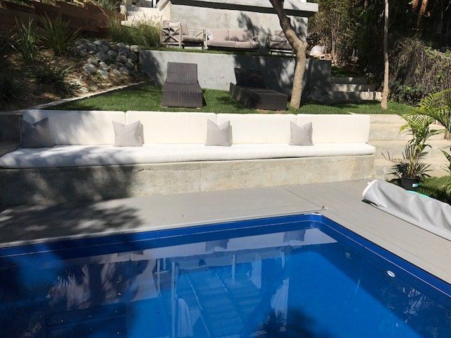 Poolside concrete seating with cream cushions and pillows, overlooking a pool.