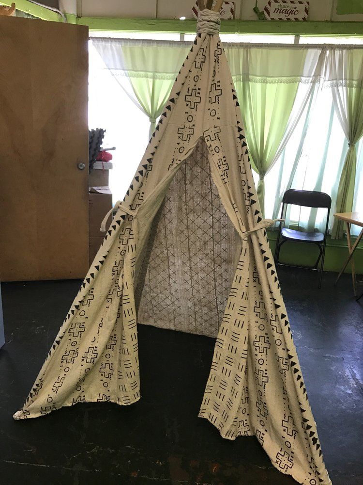 A-frame play tent with black patterned design; inside, a light patterned interior; on a green floor.
