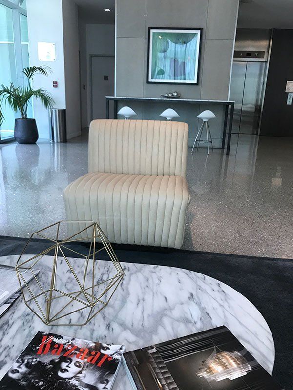 Lobby seating area: Cream-colored chair, marble coffee table with books, geometric gold object, and a framed art piece.