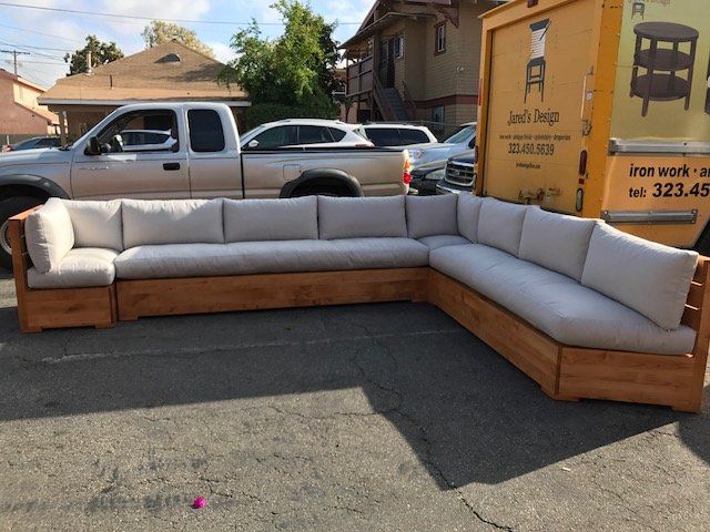 Large wooden sectional sofa with gray cushions, parked on a street near a truck.