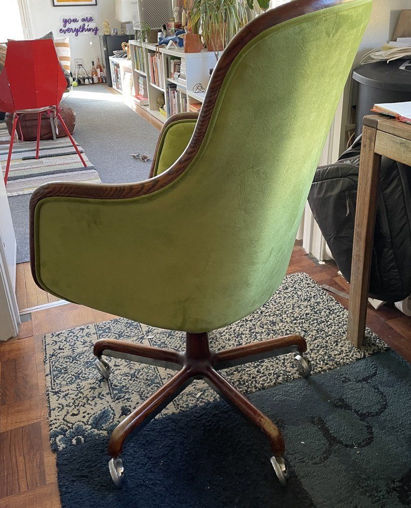 Green velvet office chair with wood trim and base, on a patterned rug.