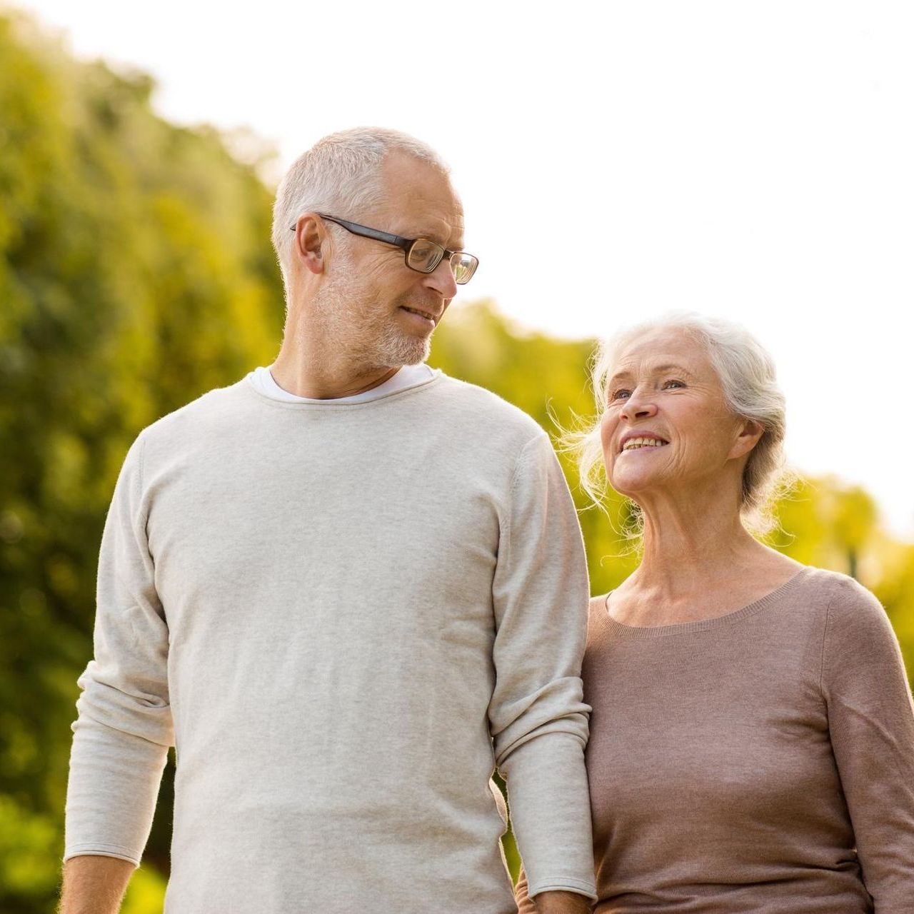 A man and a woman are walking in a park holding hands.