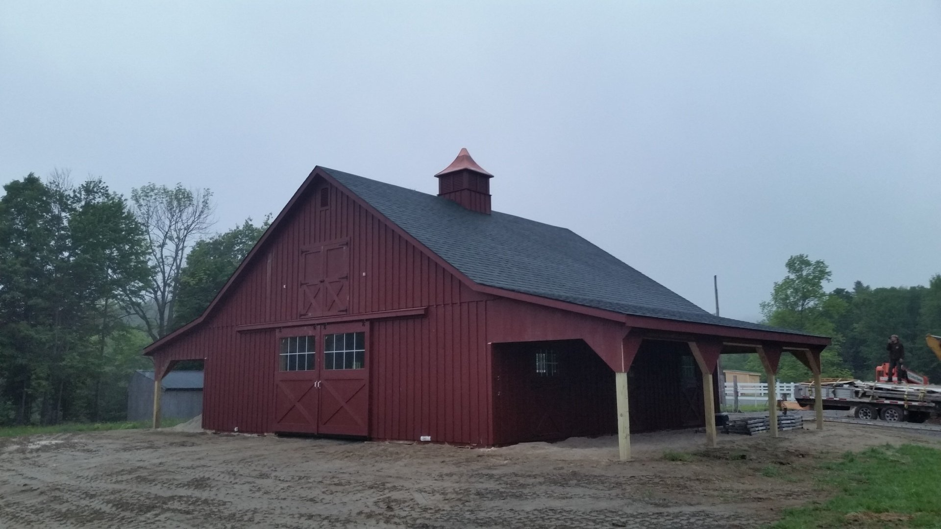A red barn with a black roof is sitting in the middle of a dirt field.