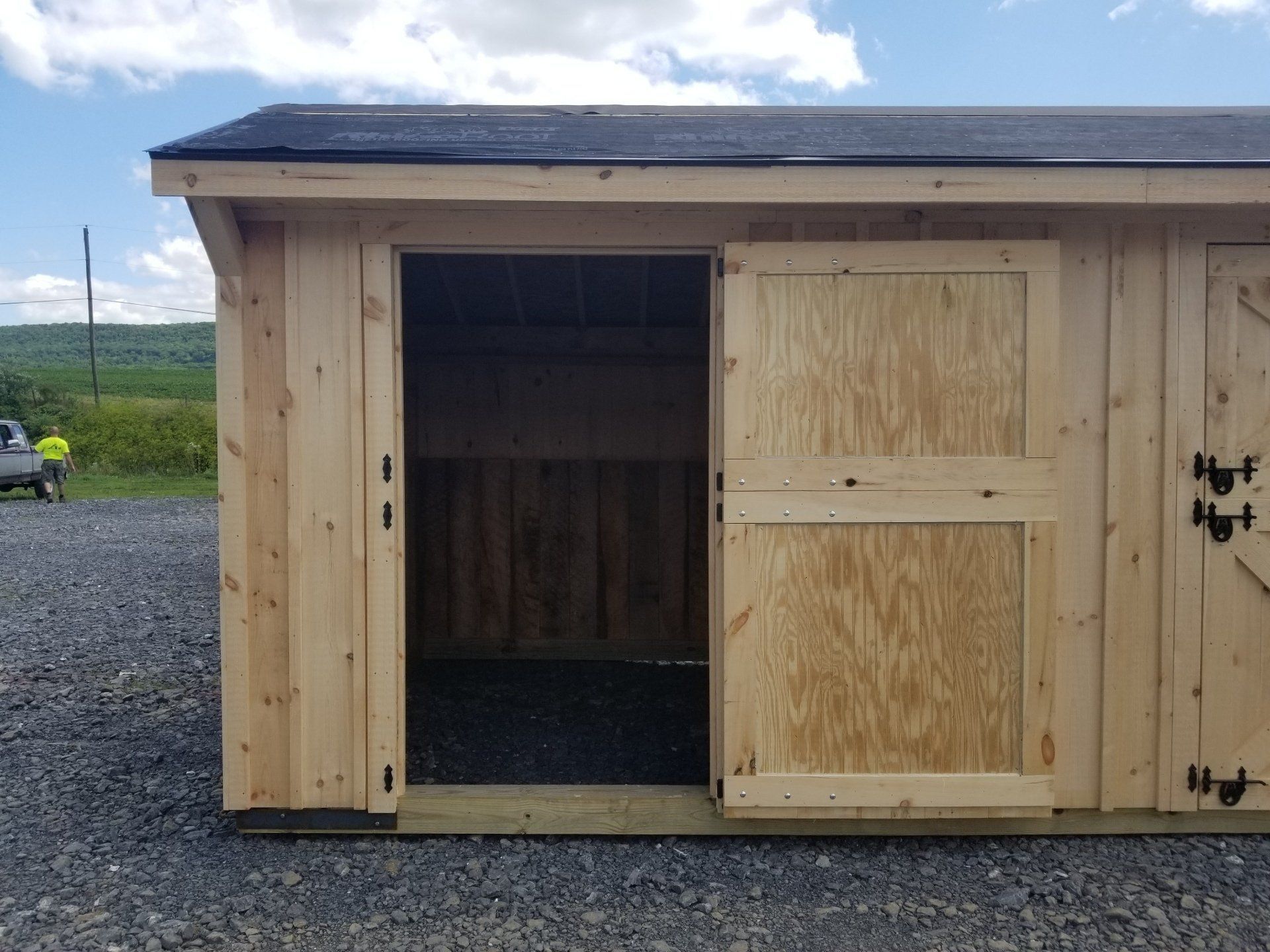 A wooden shed with a black roof and sliding doors.
