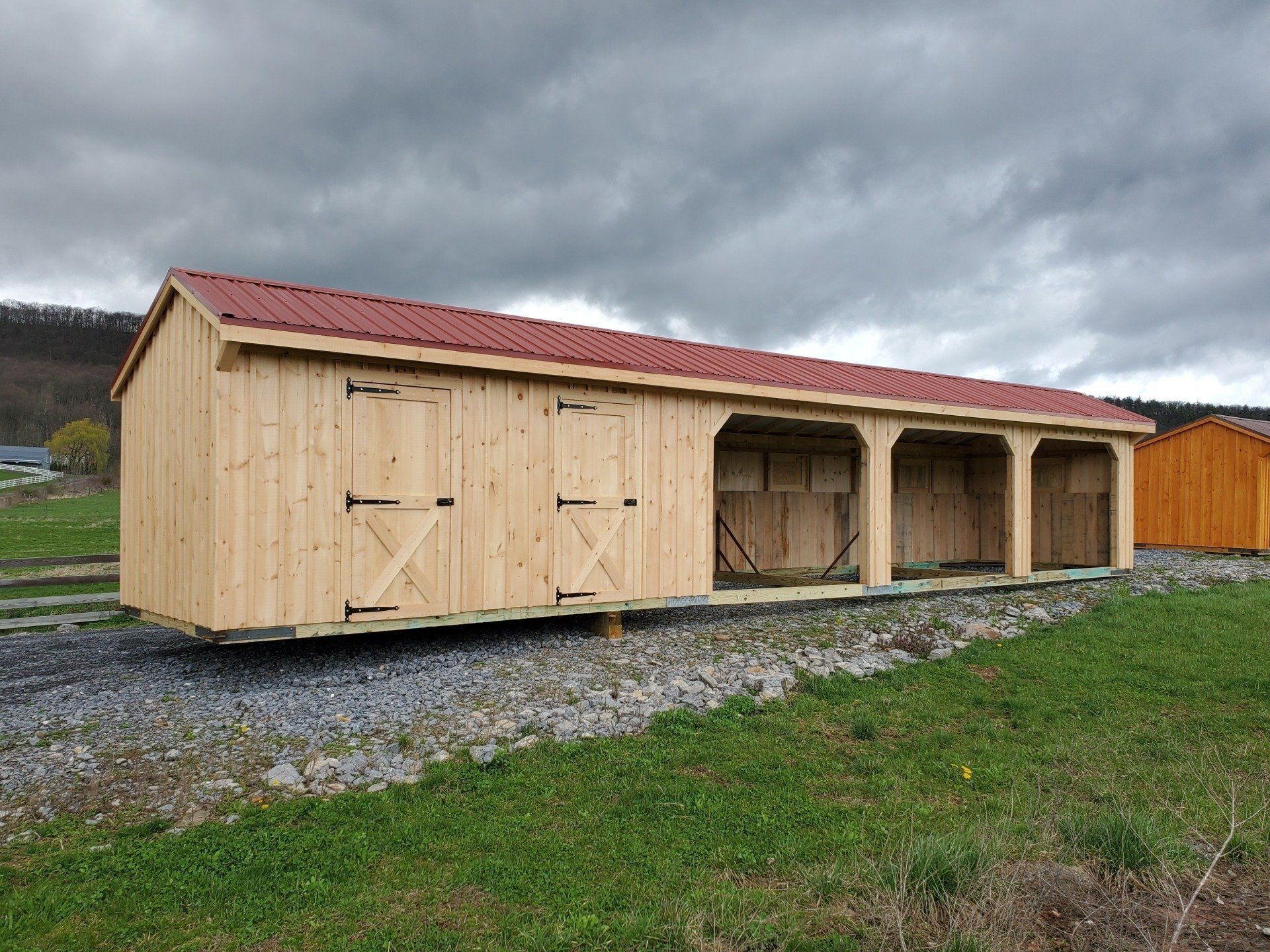A wooden shed with a red roof is sitting in a grassy field.