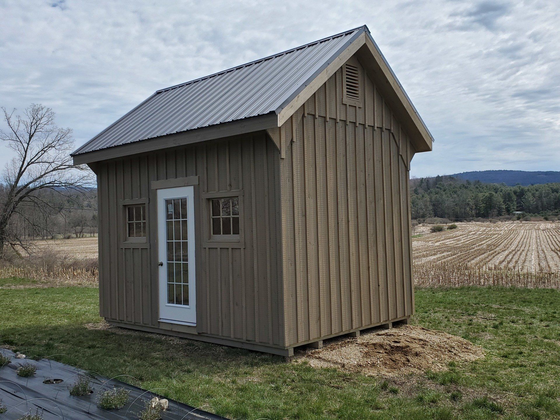 A small wooden shed with a metal roof is in the middle of a field.