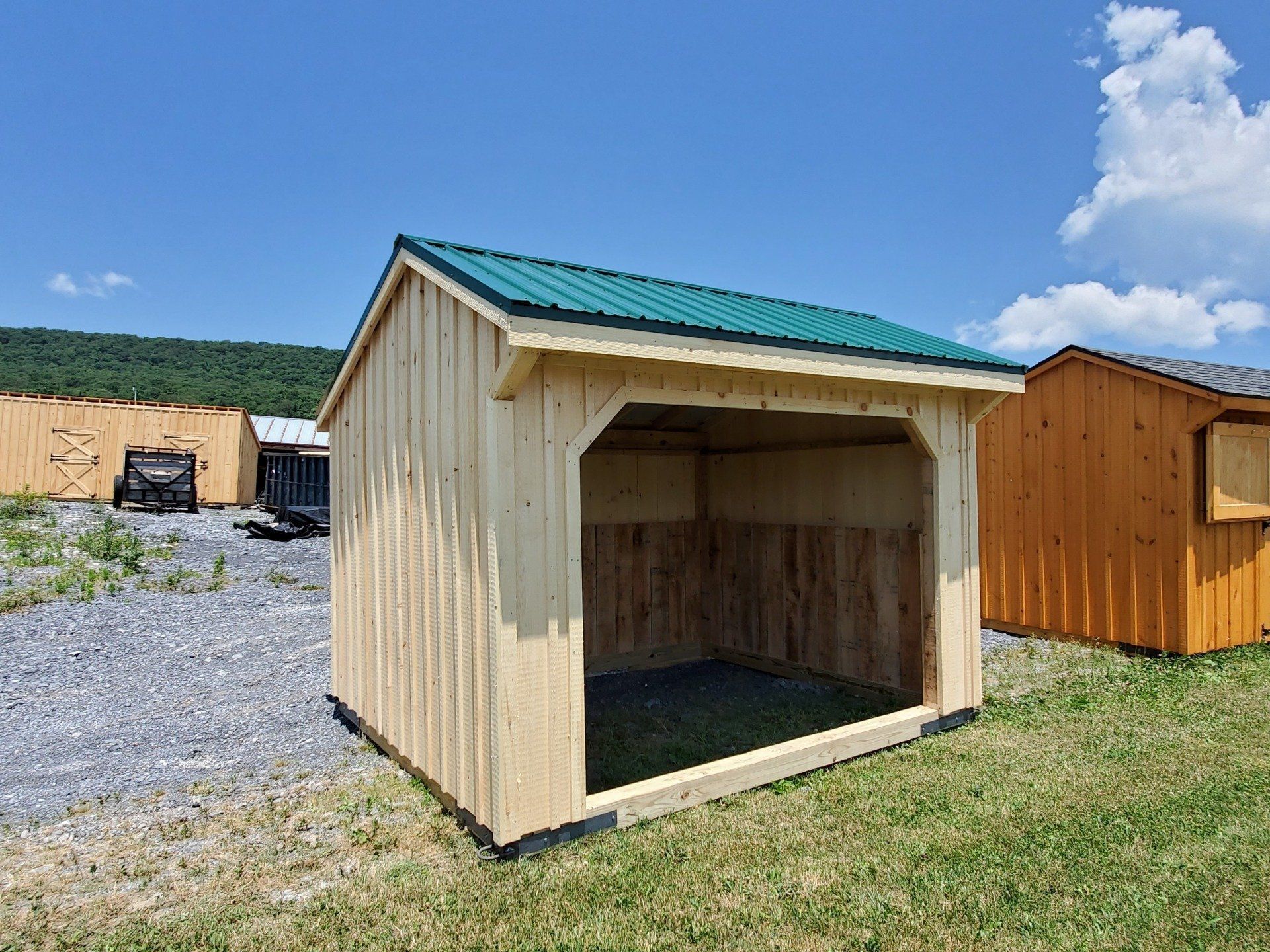 A small wooden shed with a green roof is sitting in a grassy field.