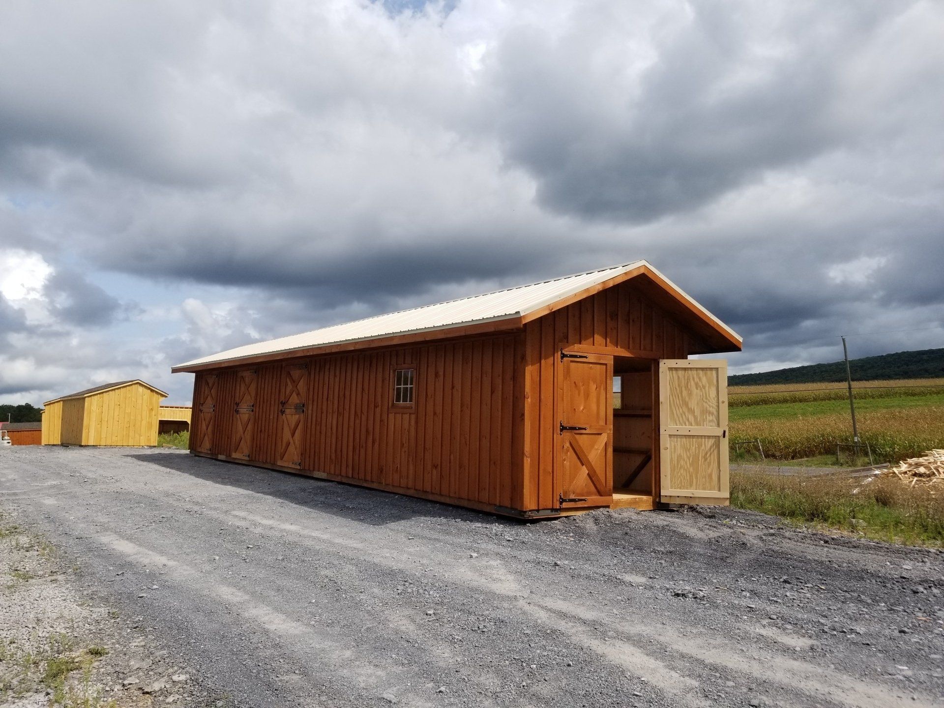 A wooden shed is sitting on the side of a dirt road.