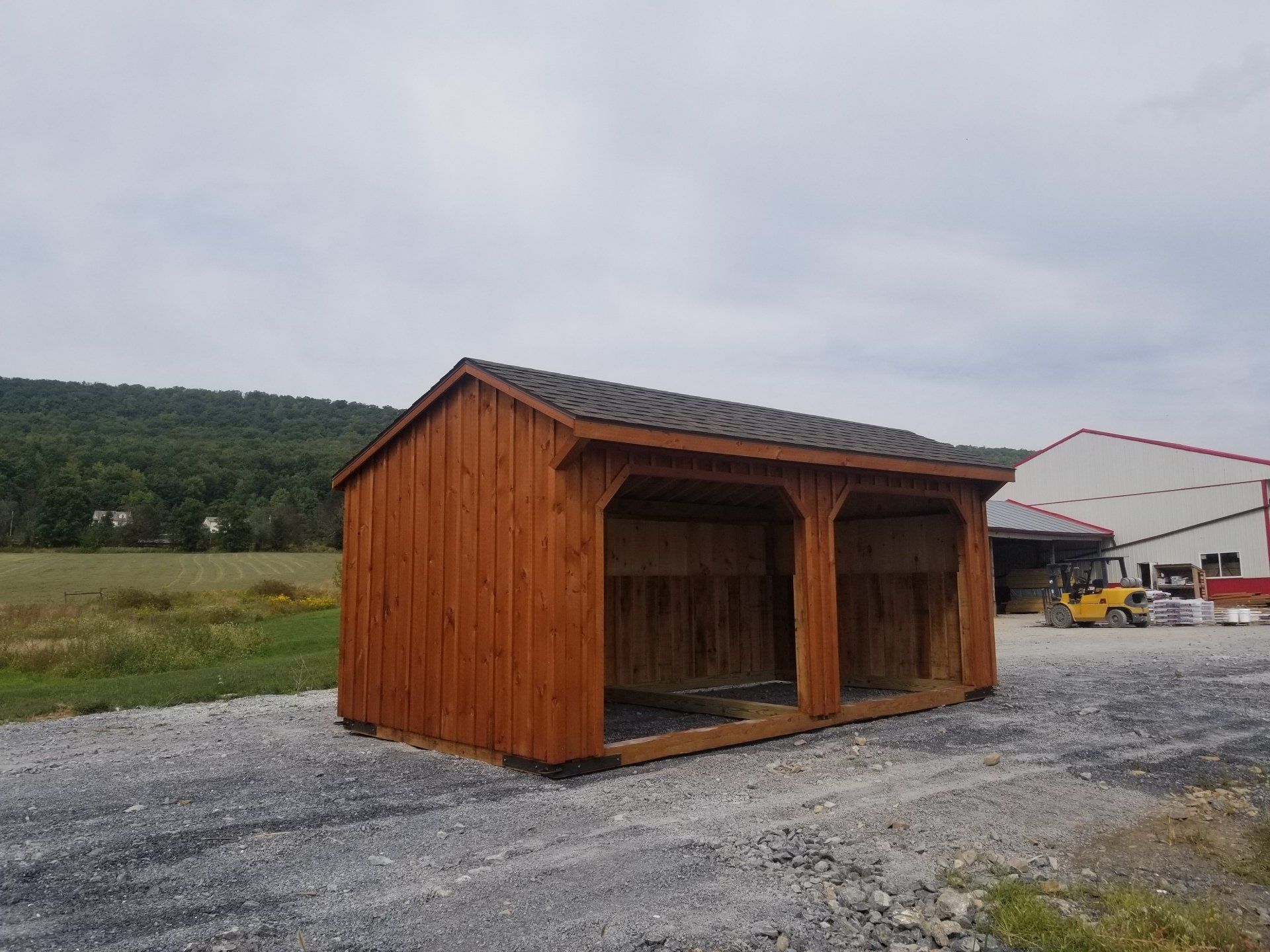 A wooden shed is sitting in a gravel lot in front of a building.