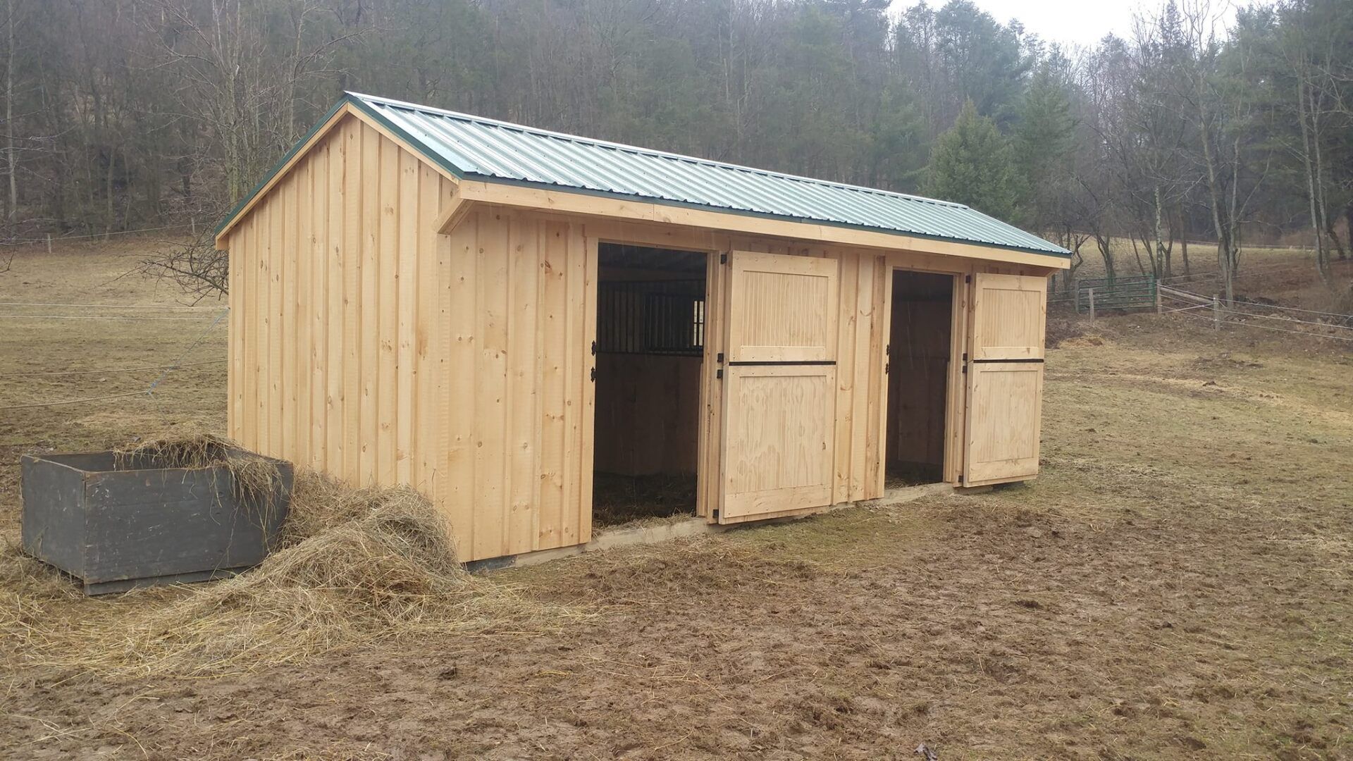 A wooden shed is sitting in the middle of a field.