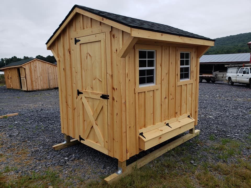 A small wooden shed with two windows is sitting in a gravel lot.
