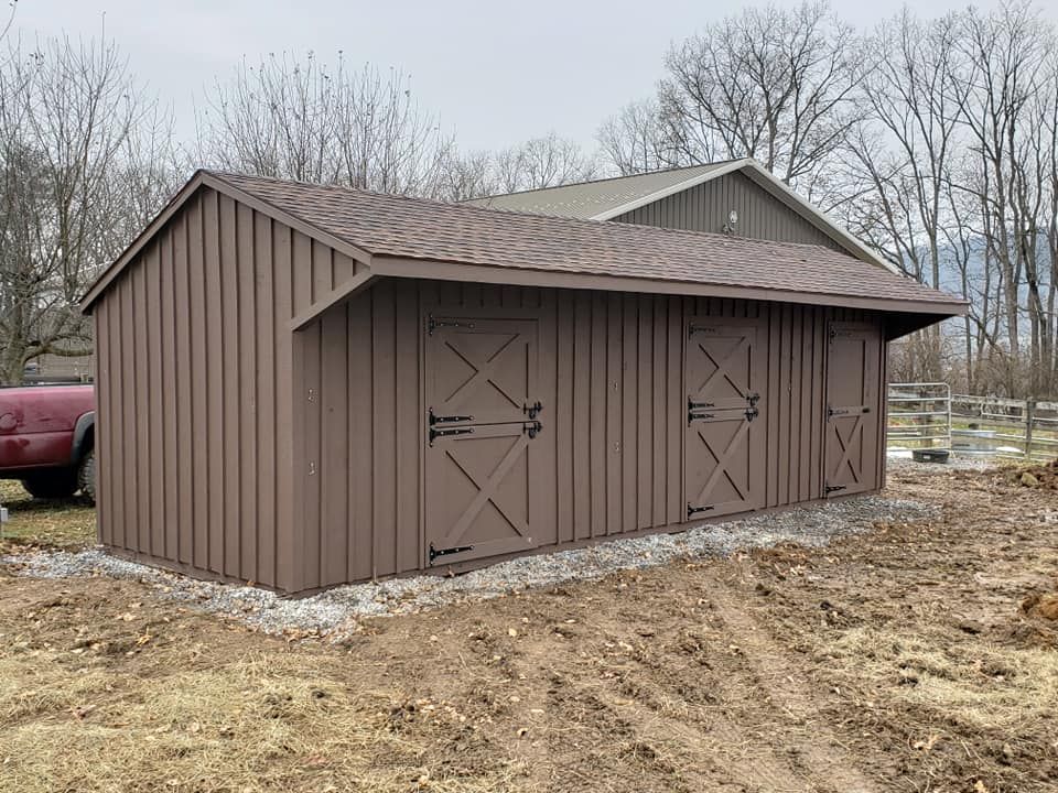A brown shed is sitting in the middle of a dirt field.