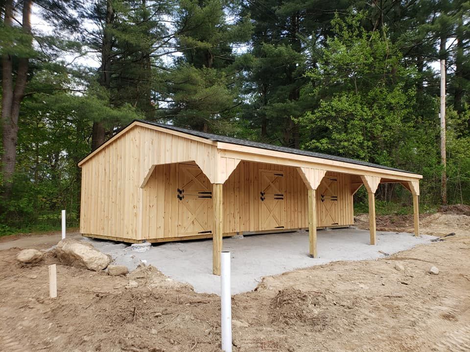A wooden shed with a canopy is sitting in the middle of a dirt field.
