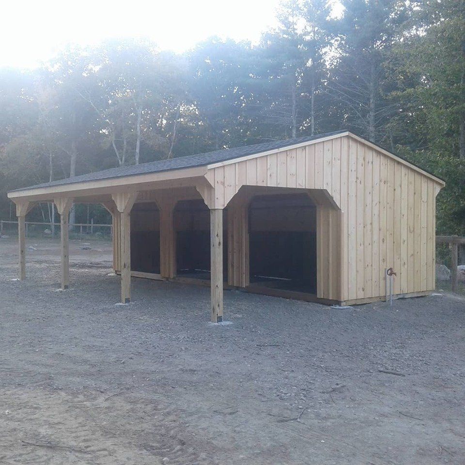 A wooden shed with a roof is sitting in the middle of a dirt field