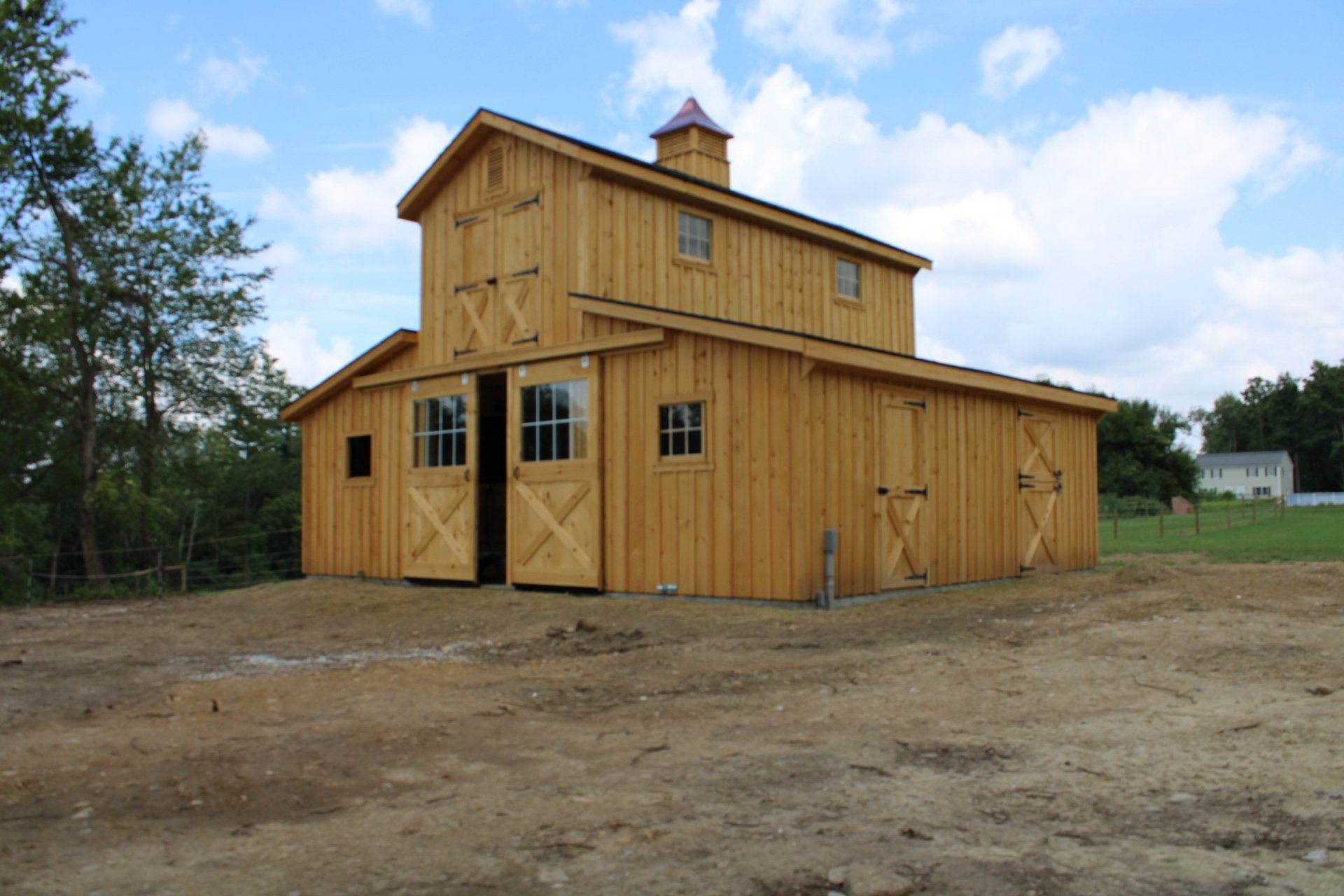 A large wooden barn is sitting in the middle of a dirt field.