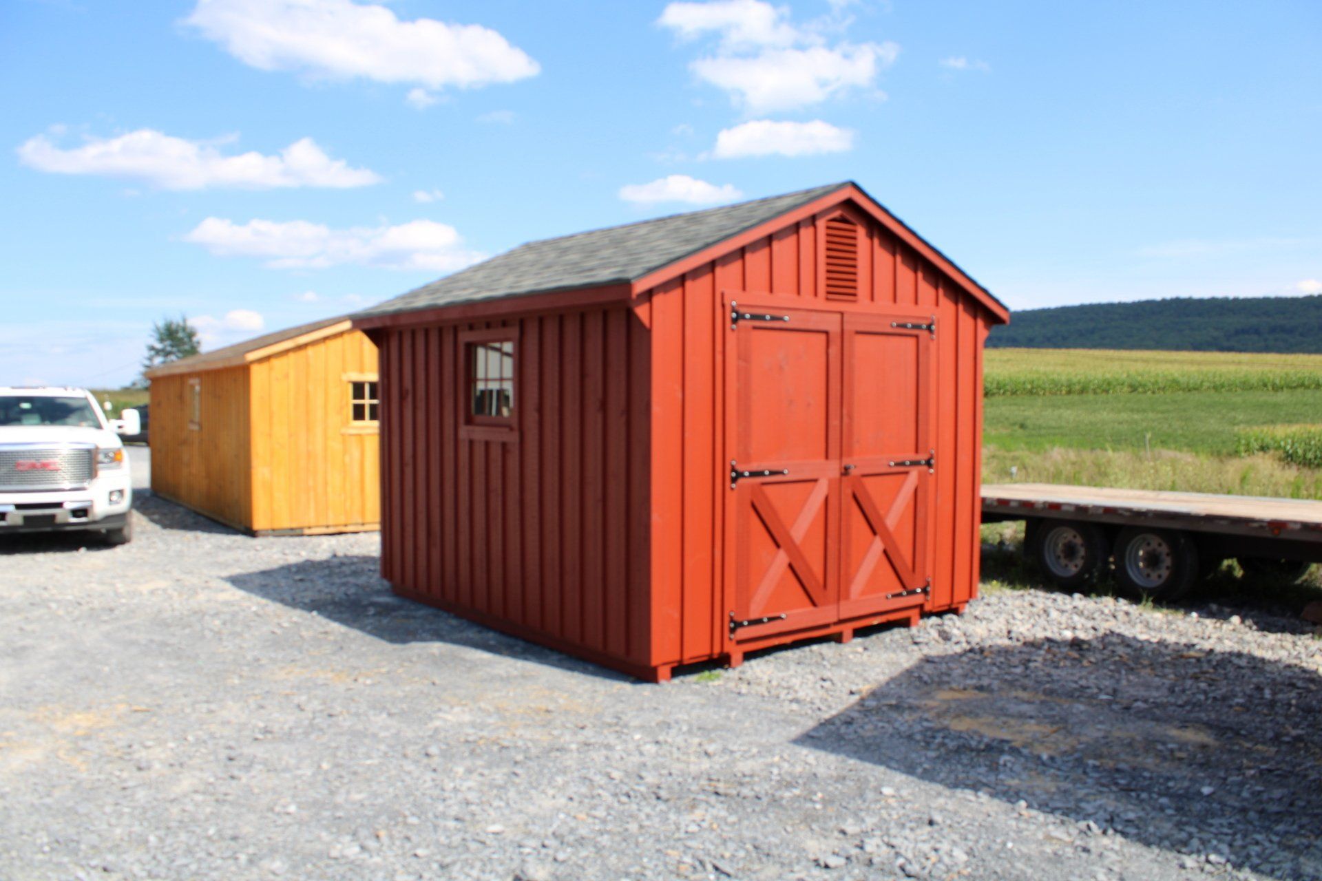 A red shed is sitting next to a yellow shed in a gravel lot.