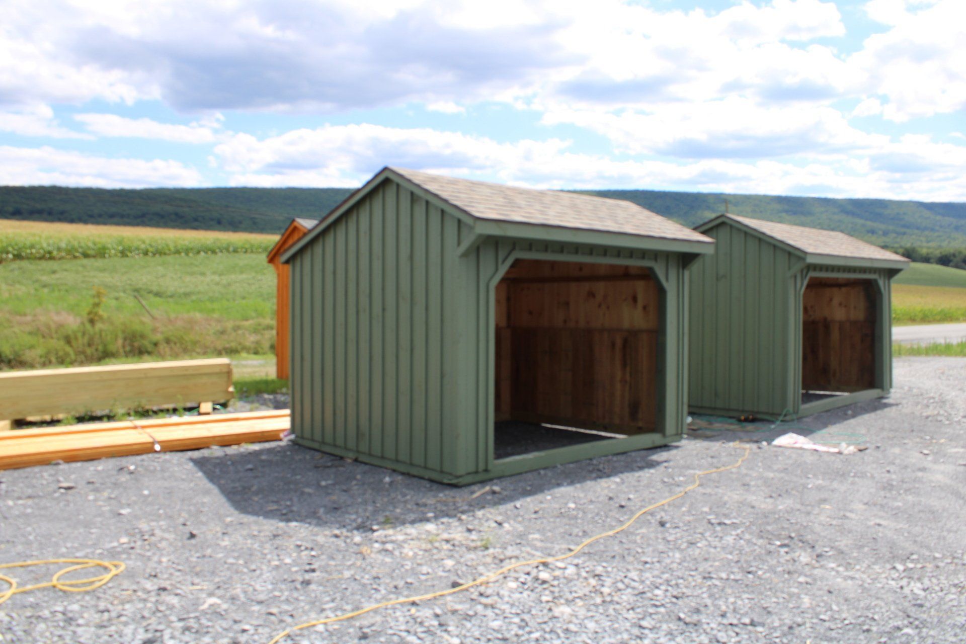 Two green sheds are sitting next to each other in a gravel lot.