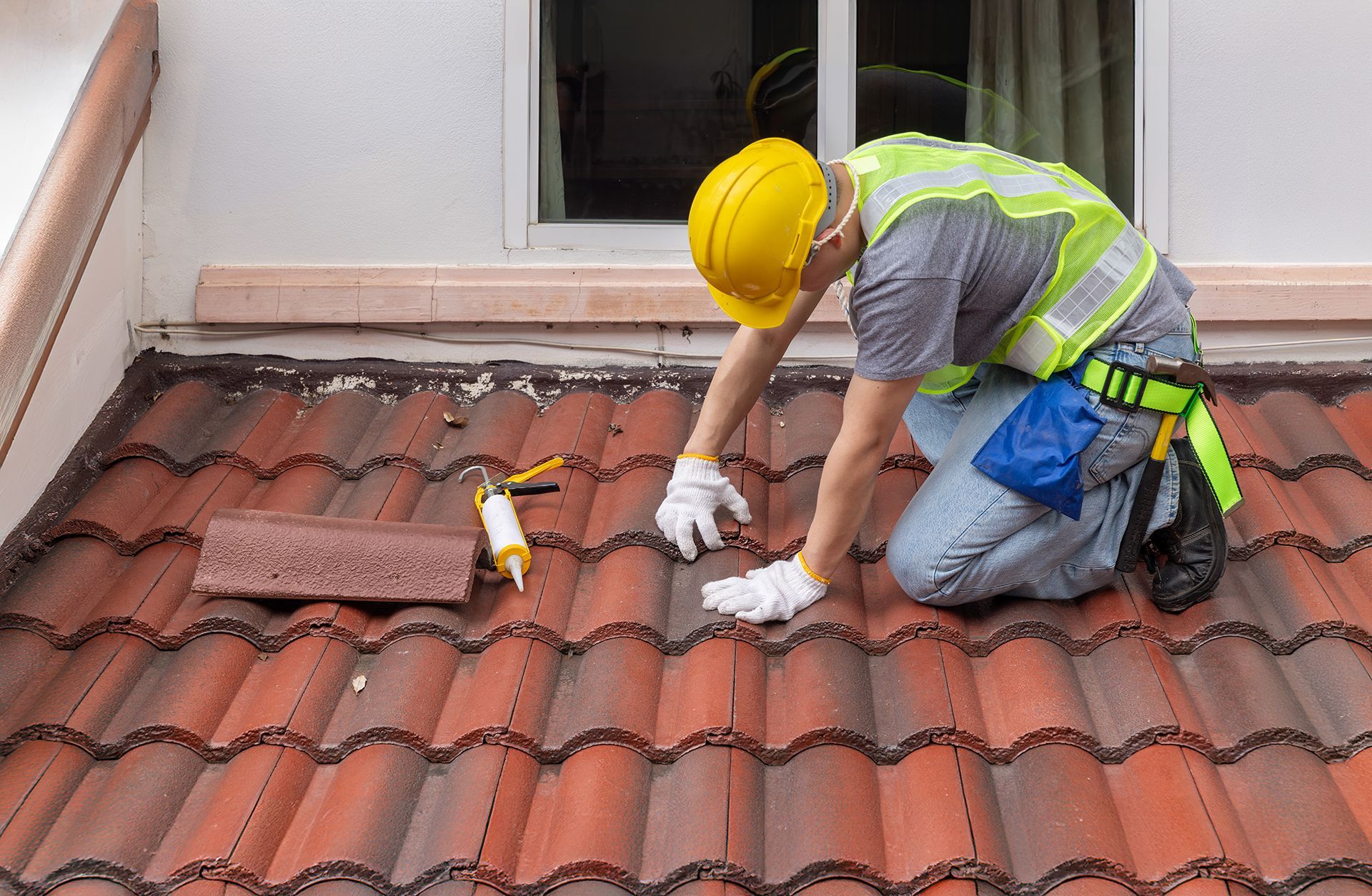 A man wearing a hard hat and safety vest is working on a tiled roof.