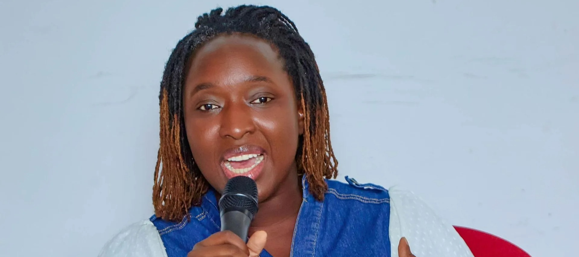 Une personne aux cheveux tressés parle dans un micro, assise à côté d'une maquette anatomique multic