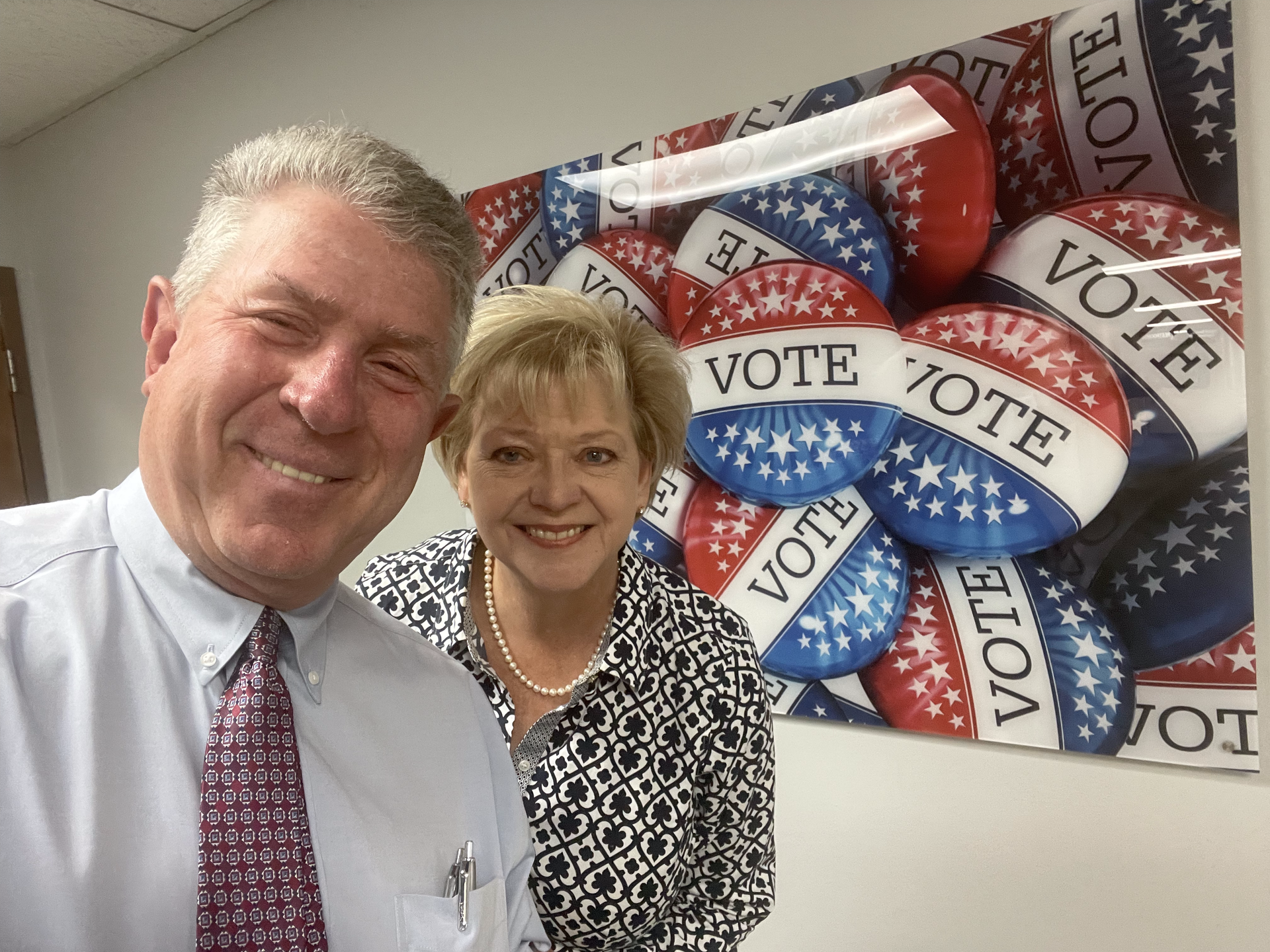A man and a woman are posing for a picture in front of a poster that says vote