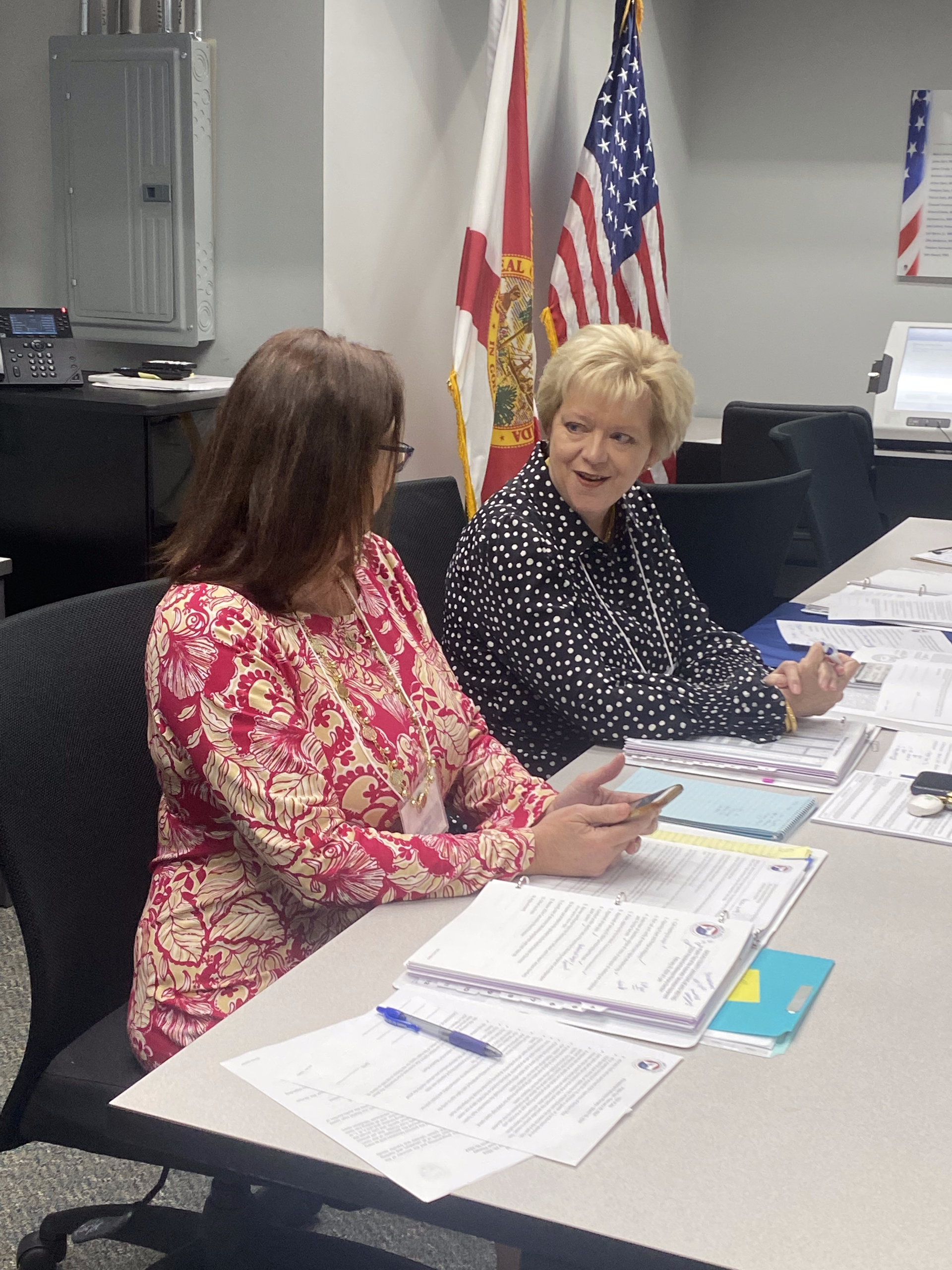 Two women are sitting at a table with american flags in the background