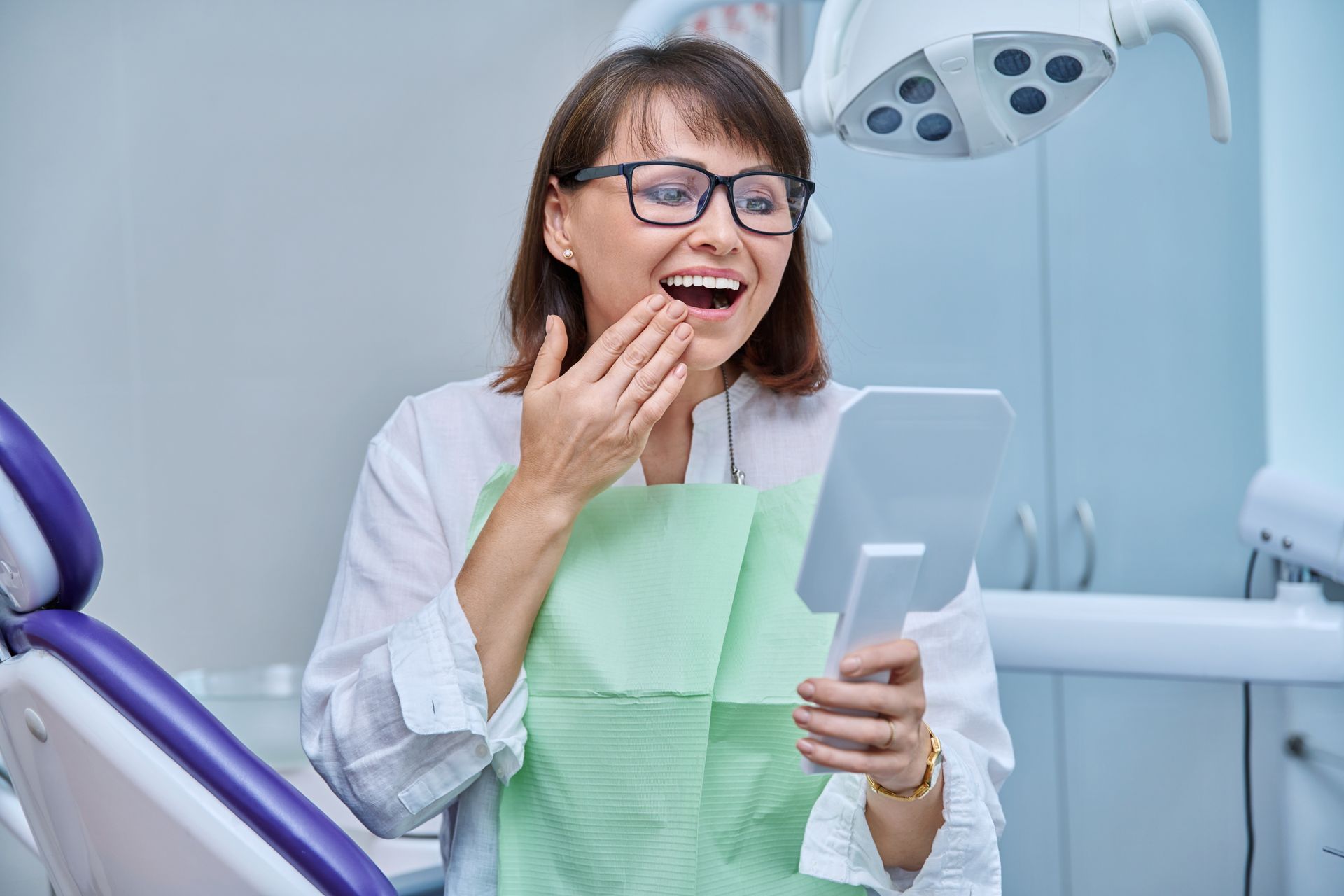 women smiling in mirror after getting dental implants
