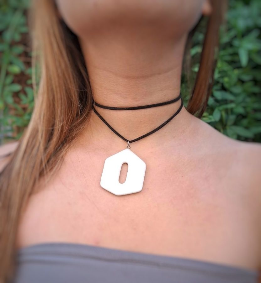Una mujer que lleva una gargantilla con un colgante blanco con la letra o.