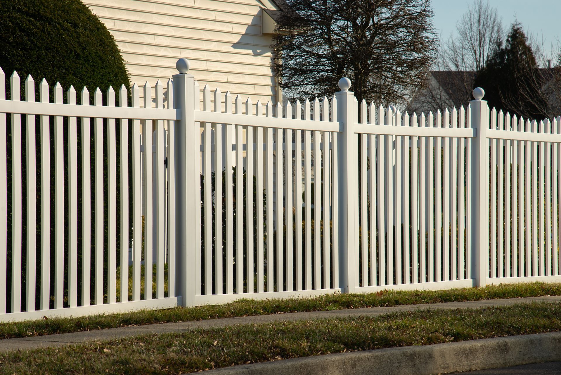 White picket fence and gate alongside a sidewalk, surrounding a property.