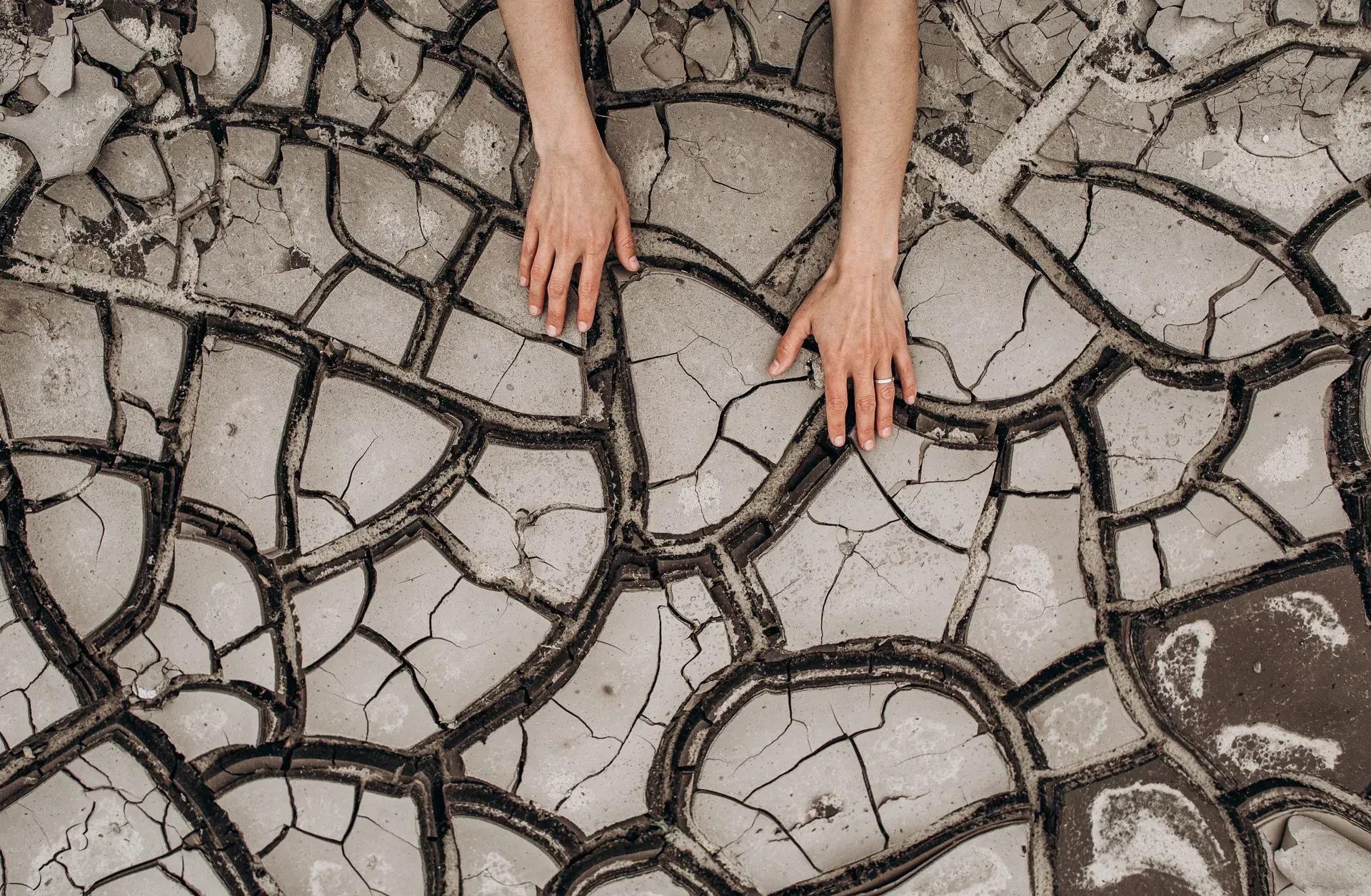 Hands resting on cracked, dry earth, suggesting aridity and hardship.
