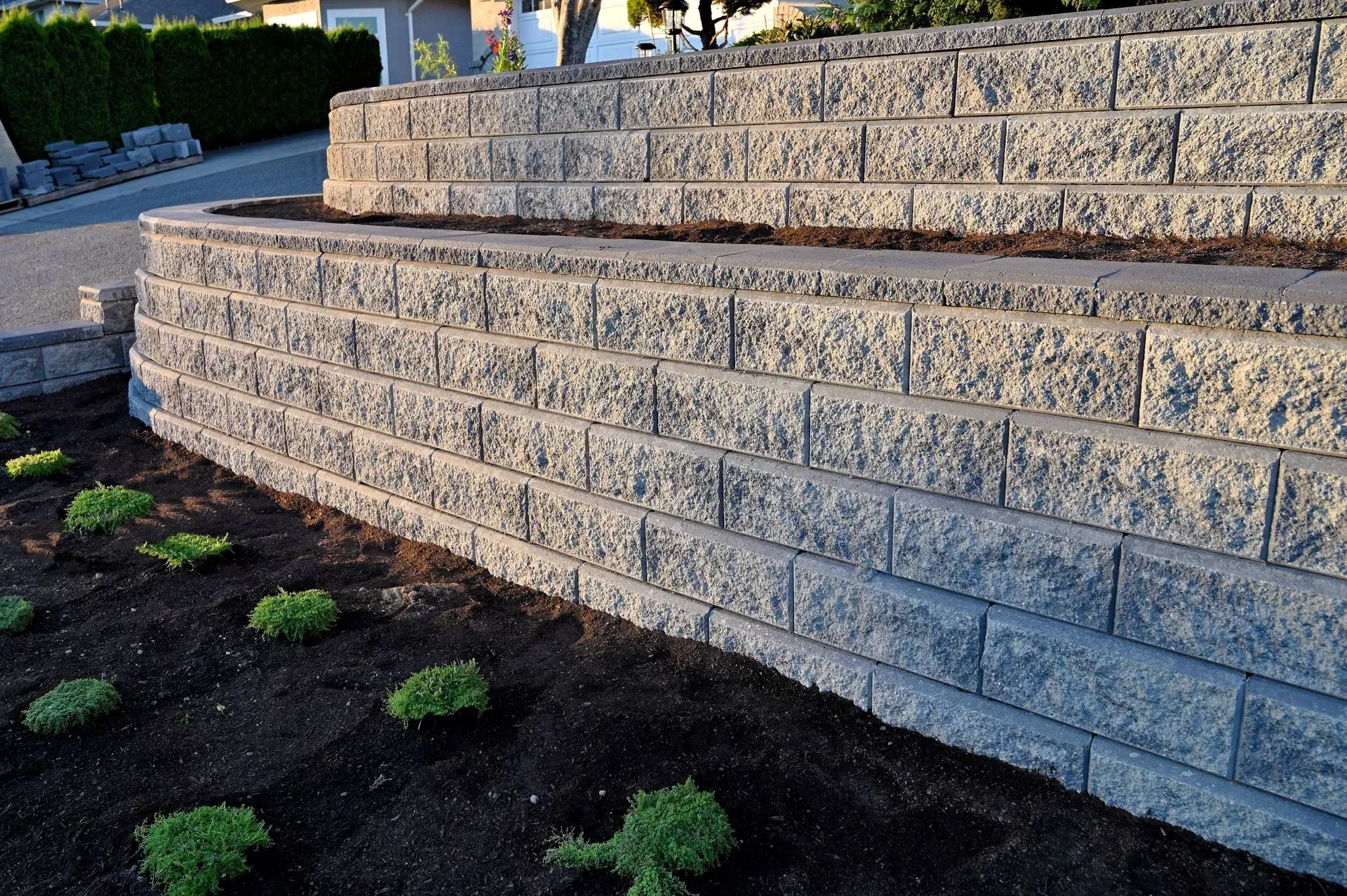 Stone retaining wall with tiered levels and small shrubs in front.