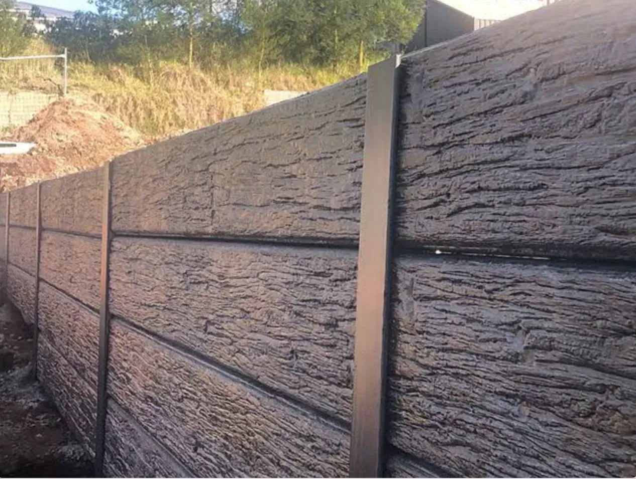 Gray textured concrete fence with black vertical posts, outdoors.