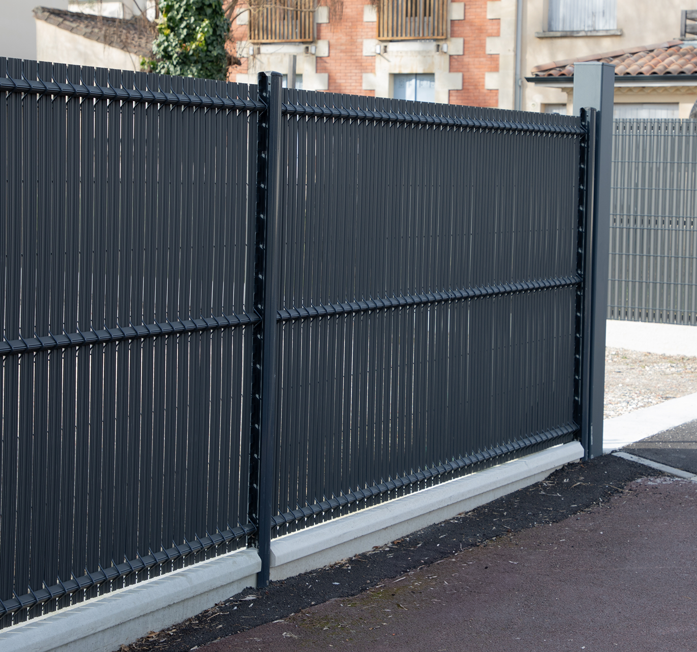 A black fence is surrounding a driveway in front of a building