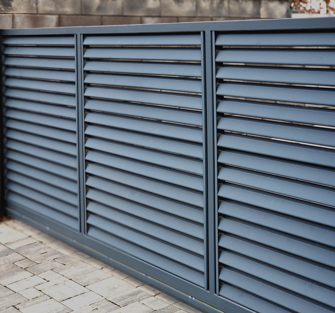 A blue fence with shutters on it is sitting on a brick sidewalk.