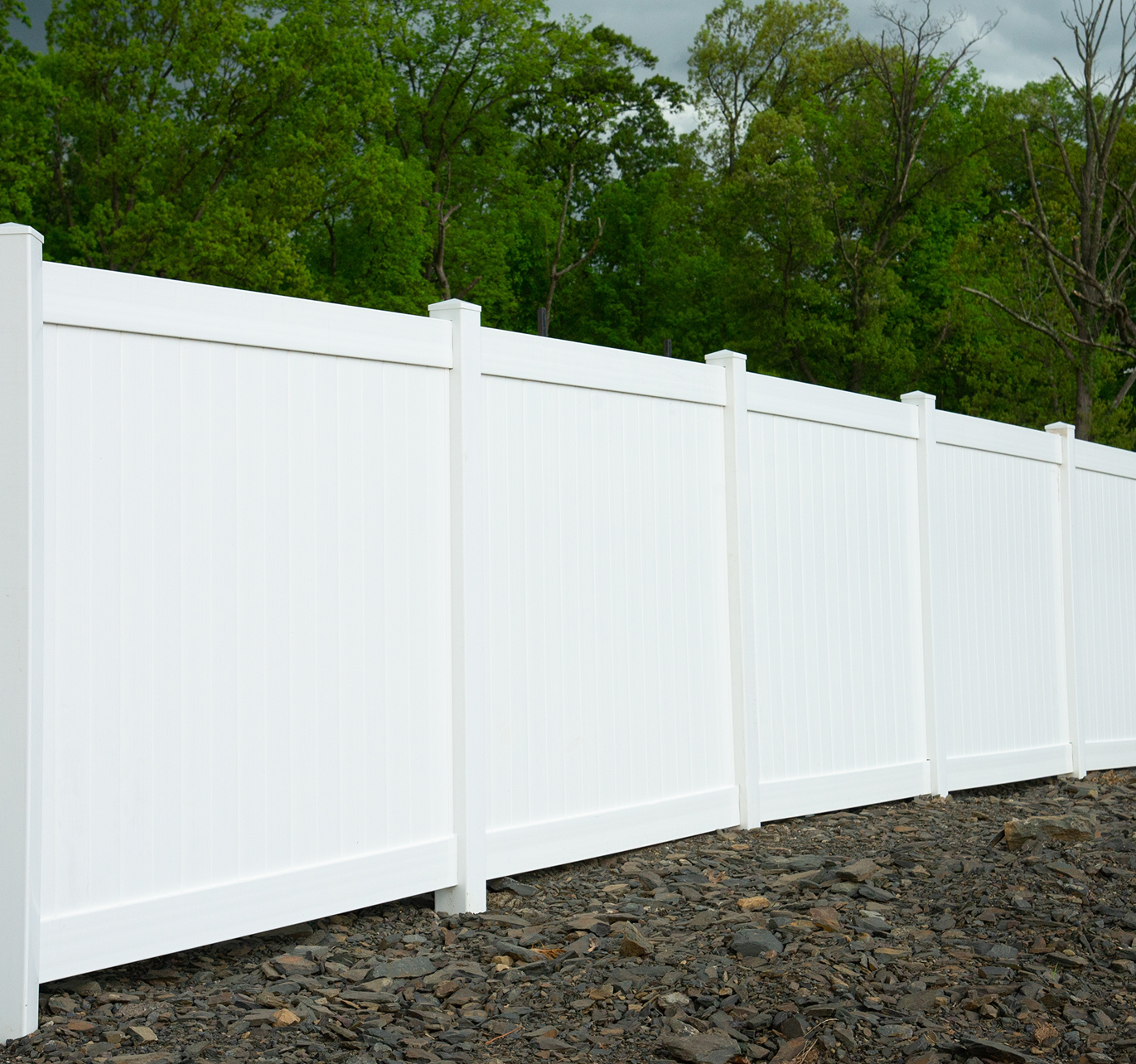 A white fence surrounds a gravel area with trees in the background.