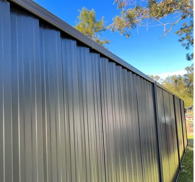 Dark gray corrugated metal fence under a blue sky.