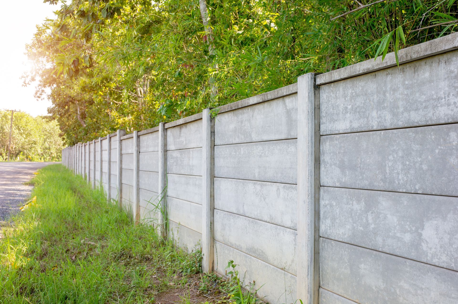 A concrete fence along a road with trees in the background.