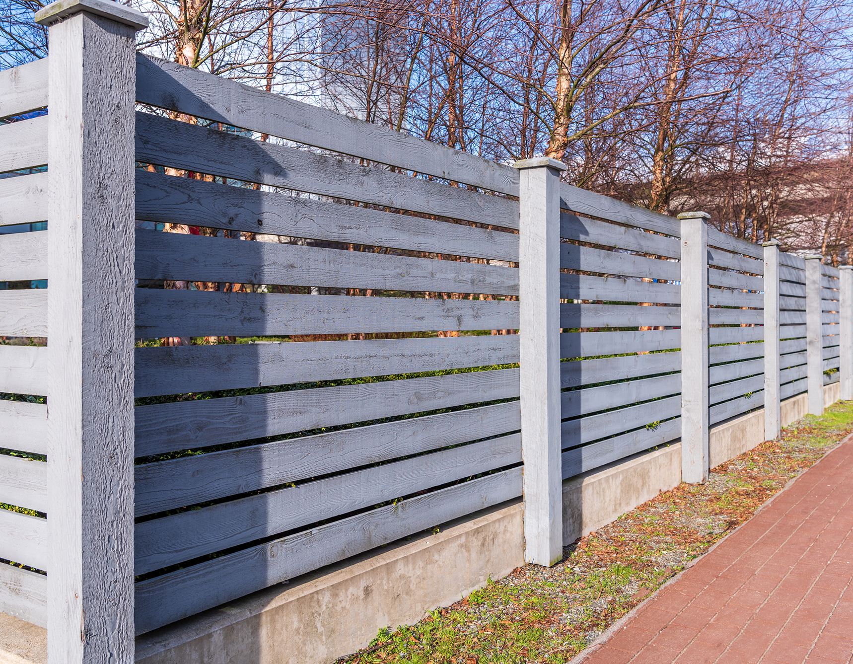 A white fence surrounds a gravel area with trees in the background.