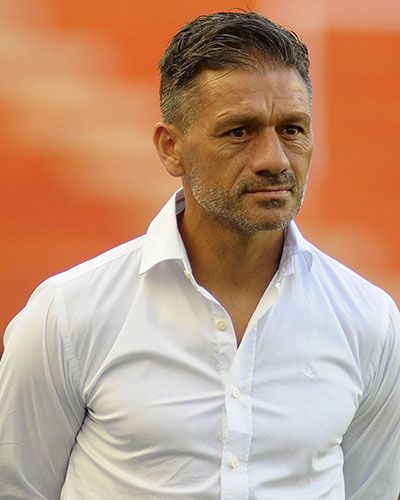 Hombre de pelo corto y gris, vestido con una camisa blanca abotonada y aspecto serio.