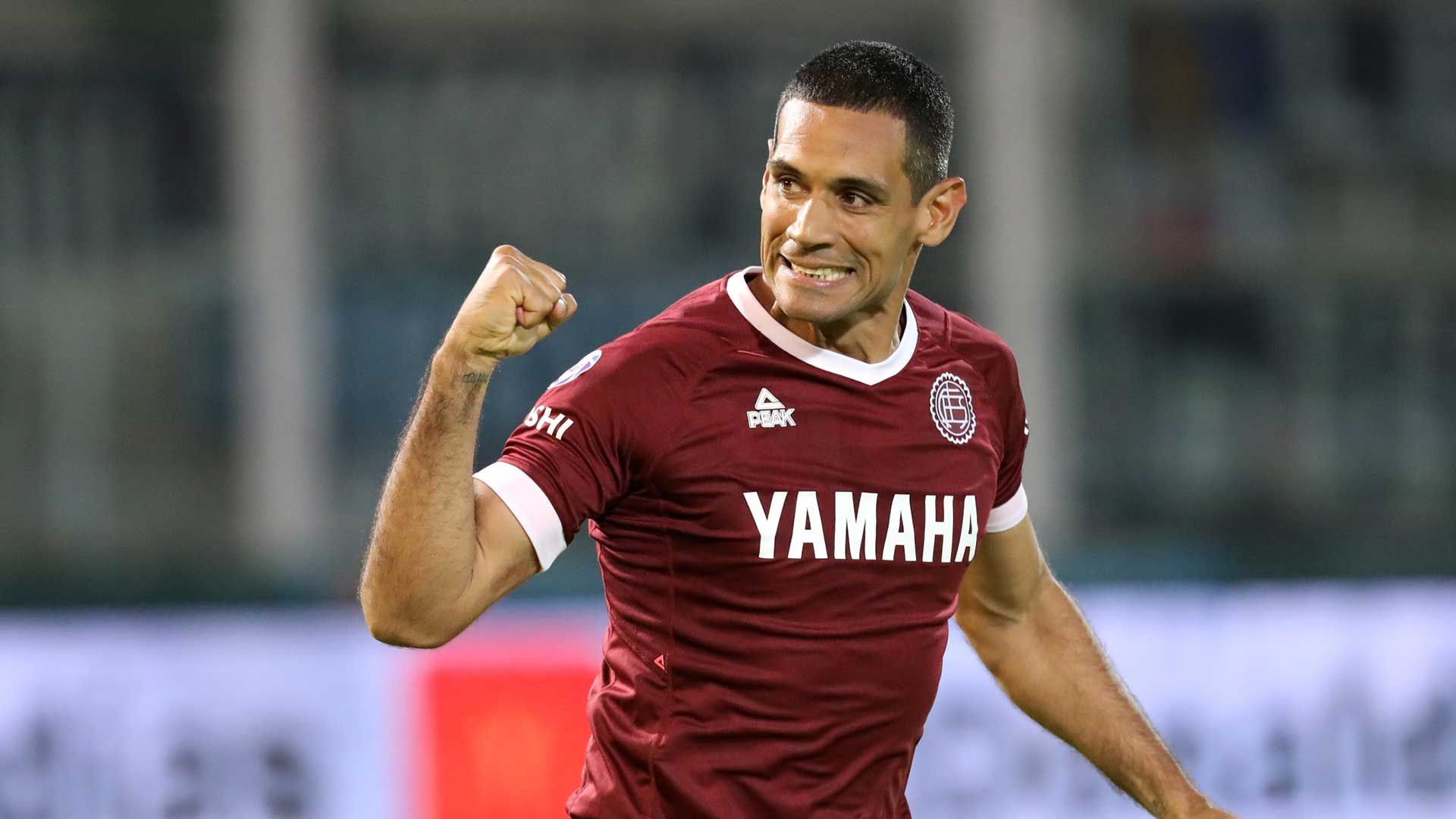 Jugador de fútbol con camiseta granate de Yamaha celebrando con el puño en alto.