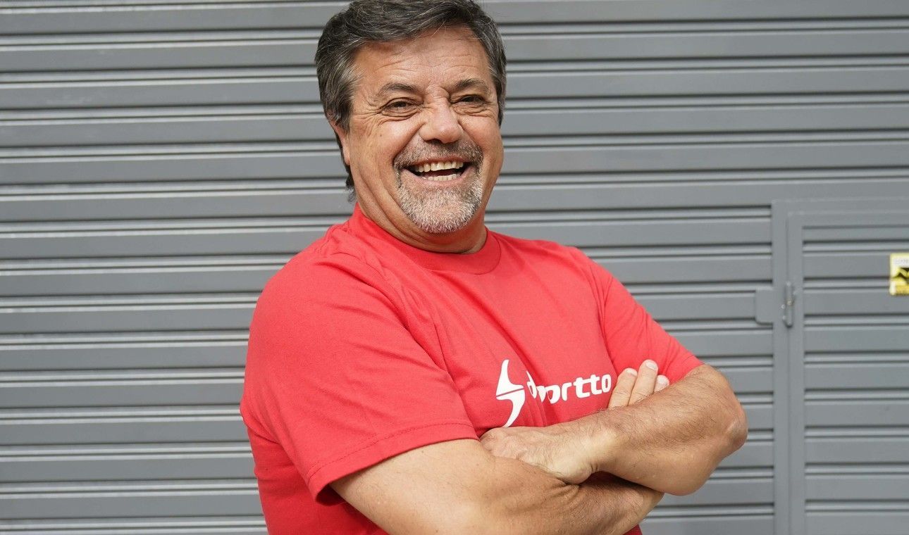 Hombre con camisa roja sonriendo, con los brazos cruzados, frente a una puerta metálica gris.