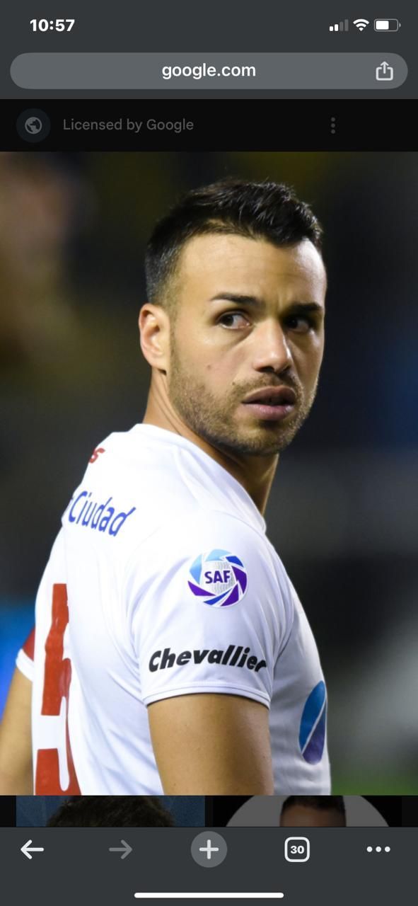 Un jugador de fútbol con una camiseta blanca mira por encima de su hombro derecho; es visible el logo del equipo.
