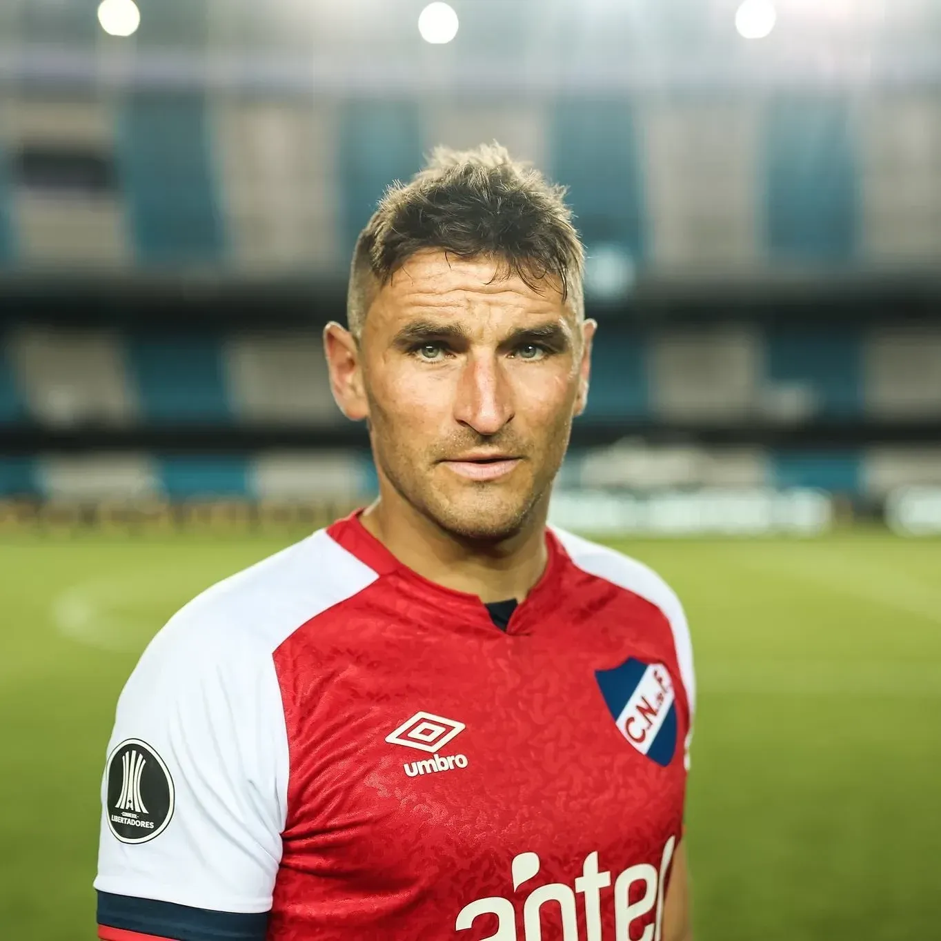 Jugador de fútbol con camiseta roja y blanca, de pie en un campo.