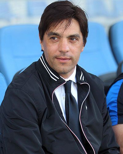 Diego Simeone con un traje negro, mirando fijamente al espectador, sobre fondo azul marino.