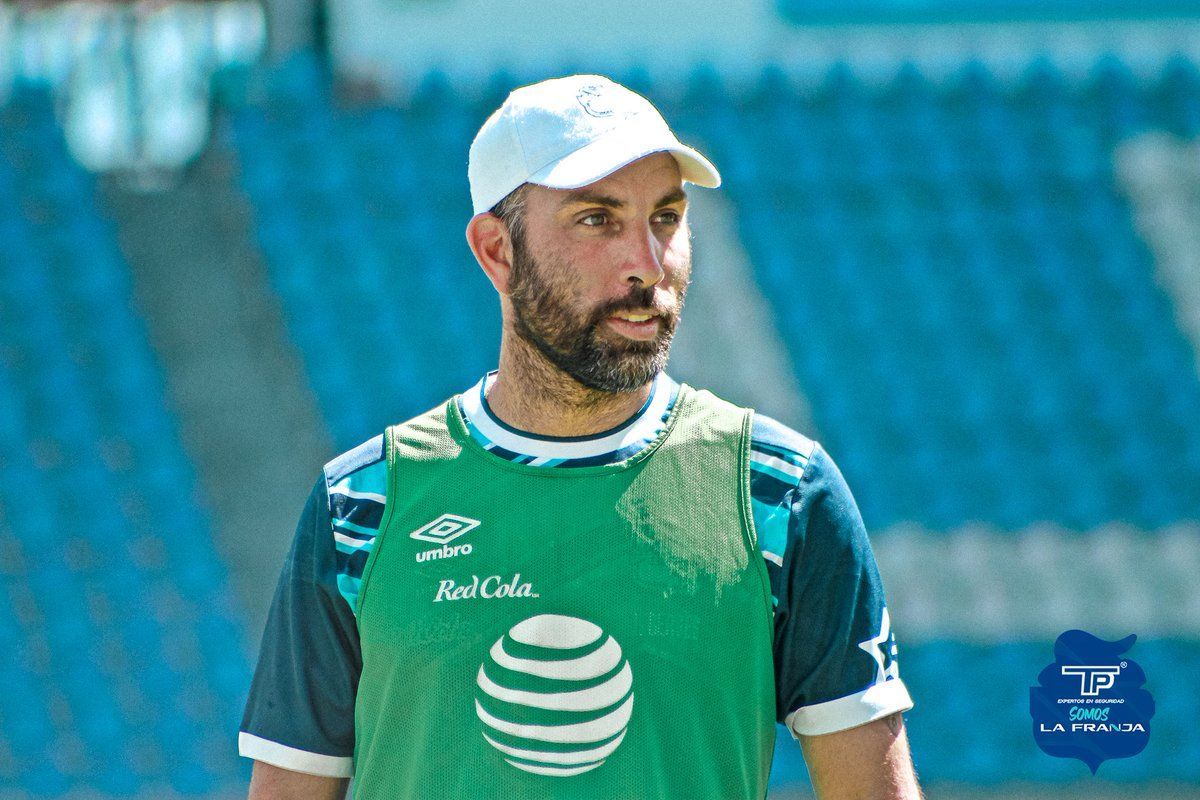 Jugador de fútbol con uniforme rojo celebrando con la boca abierta y el brazo en alto. Otro jugador de azul detrás de él.