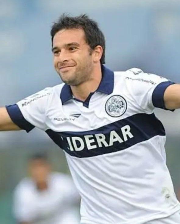 Jugador de fútbol con camiseta blanca y azul marino, celebrando con los brazos en alto.