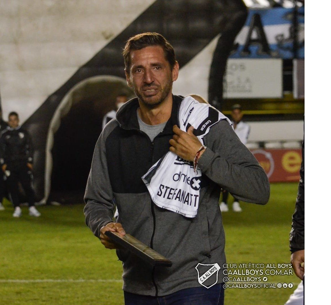 Jugador de fútbol haciendo un gesto de pulgar hacia arriba, sentado en un banco, vistiendo una camiseta blanca y negra.